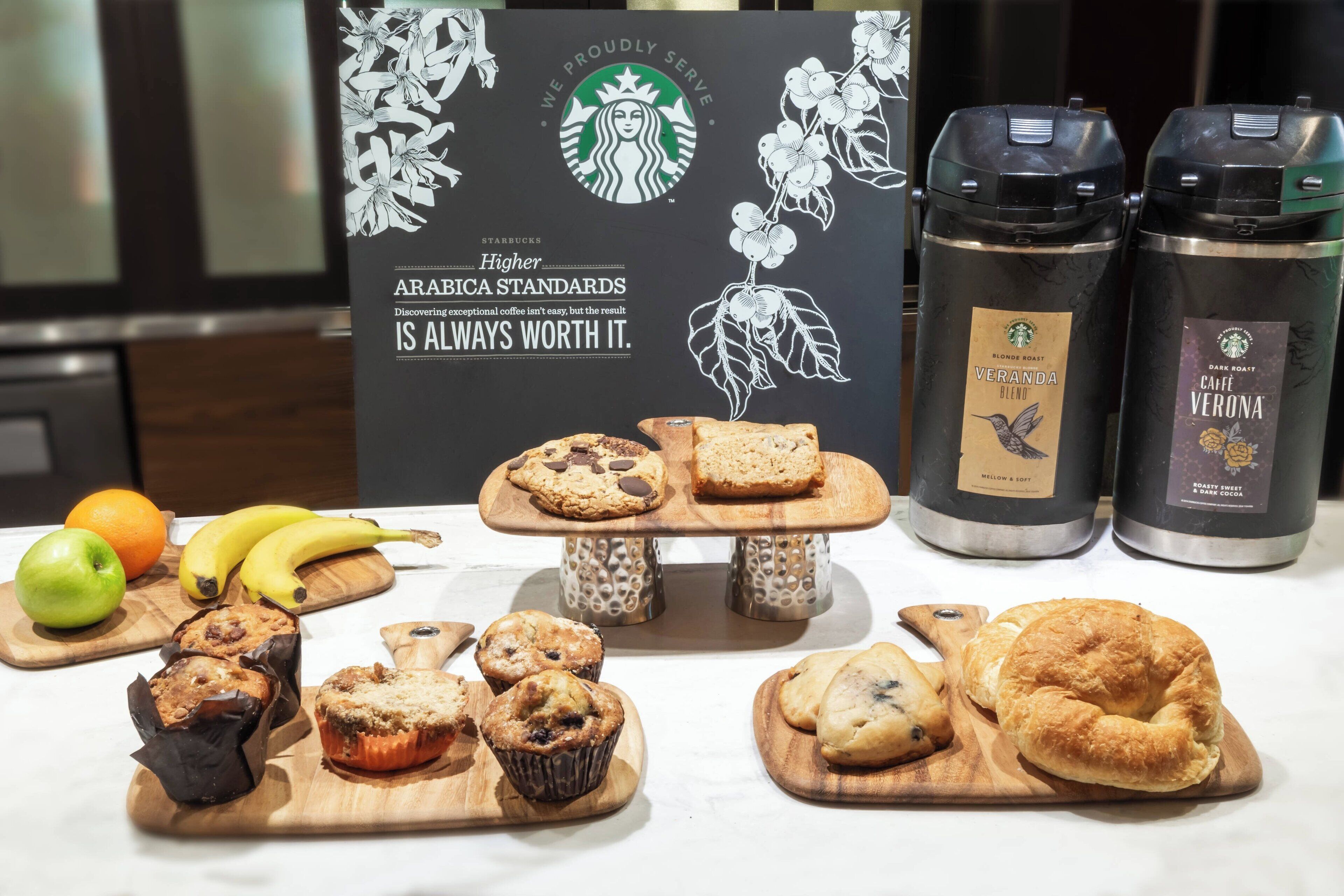 A table with pastries, a Starbucks sign, and two coffee containers.