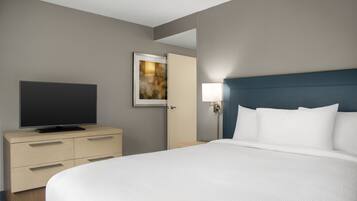 Une chambre d’hôtel avec un lit, un téléviseur posé sur une commode, un tableau accroché au mur et une table de chevet avec une lampe.
