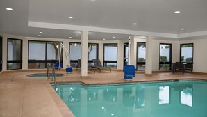 Piscina interna com água cristalina, cercada por espreguiçadeiras e um solário.