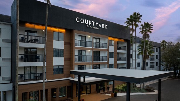 Un hotel de varios pisos llamado 'Courtyard by Marriott' con balcones, mobiliario exterior y palmeras.