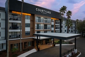 A multi-story hotel named 'Courtyard by Marriott' with balconies, outdoor seating, and palm trees. - Courtyard by Marriott Orlando East/UCF Area (Orlando)