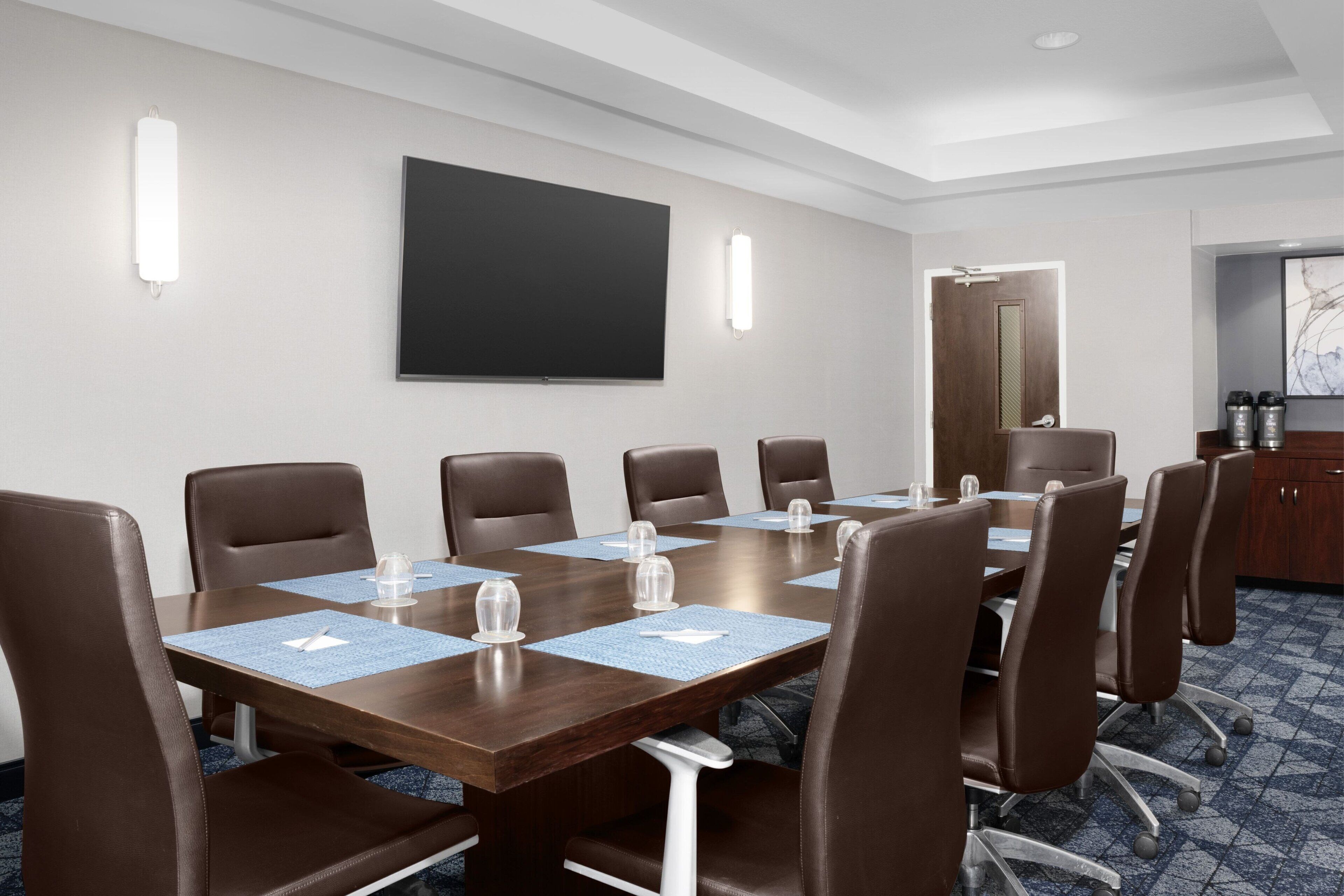 Un salón de conferencias con una gran mesa, sillas de cuero marrón y un televisor de pantalla plana en la pared.