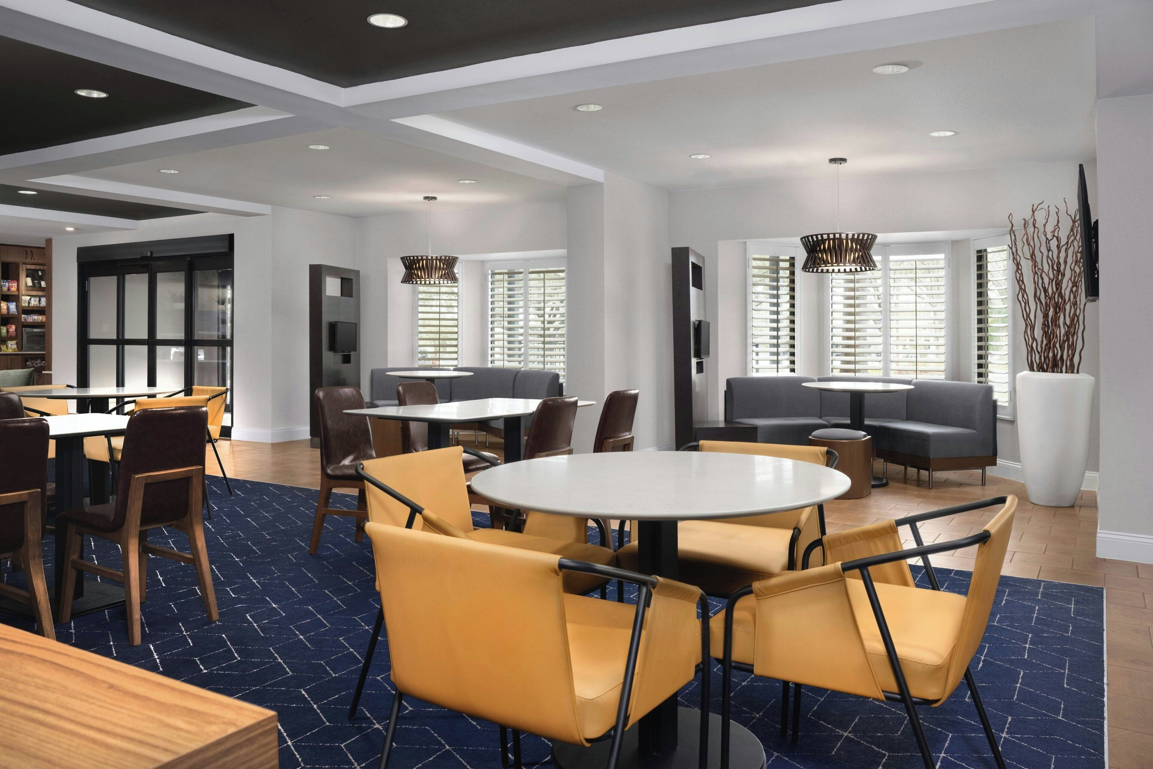A modern hotel lobby with round tables, comfortable seating, and large windows allowing natural light.