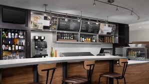 Una zona de bar moderna con una barra larga, tres taburetes, una máquina de café y una carta de vinos y cócteles.