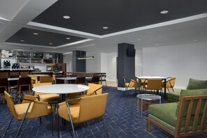 En modern hotellobby med runda bord och stolar, en bardisk och en sittgrupp med en grön soffa.