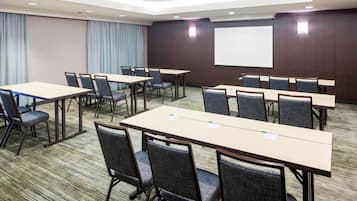 A conference room with multiple tables and chairs, a projector screen, and a large window with curtains.