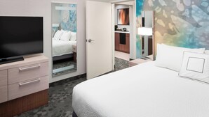 Habitación de hotel con cama, televisión, escritorio con cajones y baño visible a través de una puerta abierta.