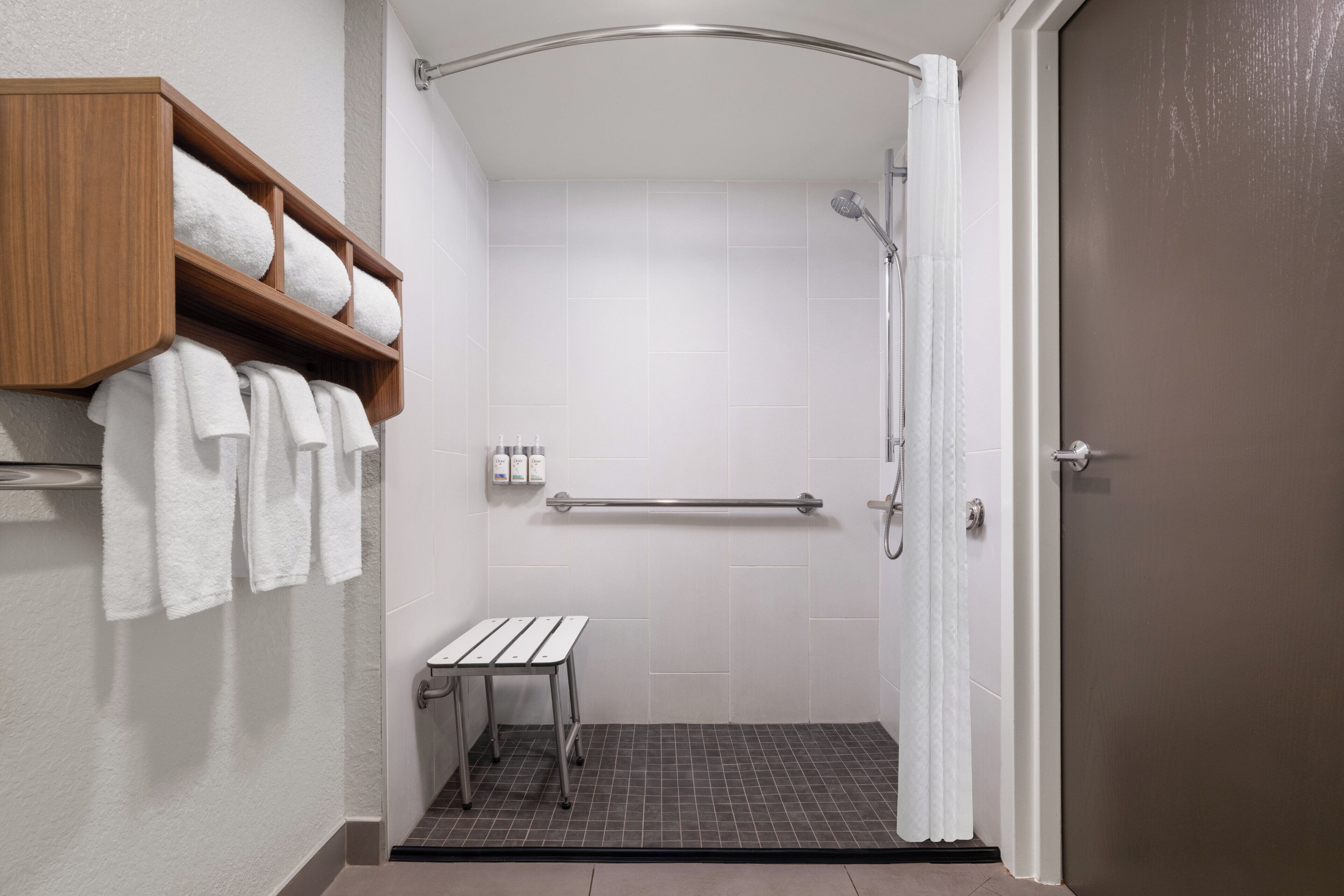 A shower with a grab bar, a bench, and a shelf with towels.