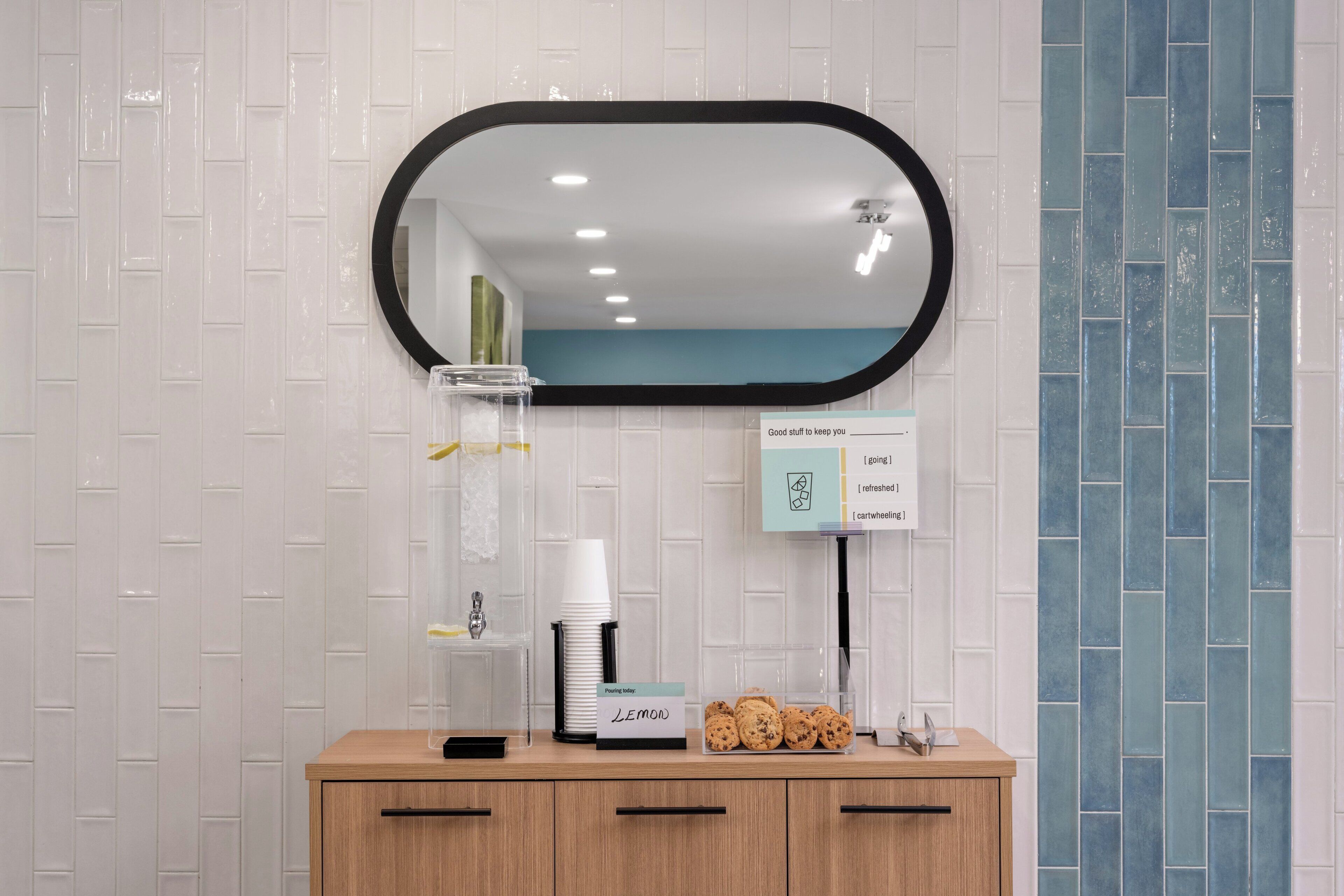 A bathroom with a mirror, a coffee machine, a sign with a lemon icon, and a cabinet with drawers.