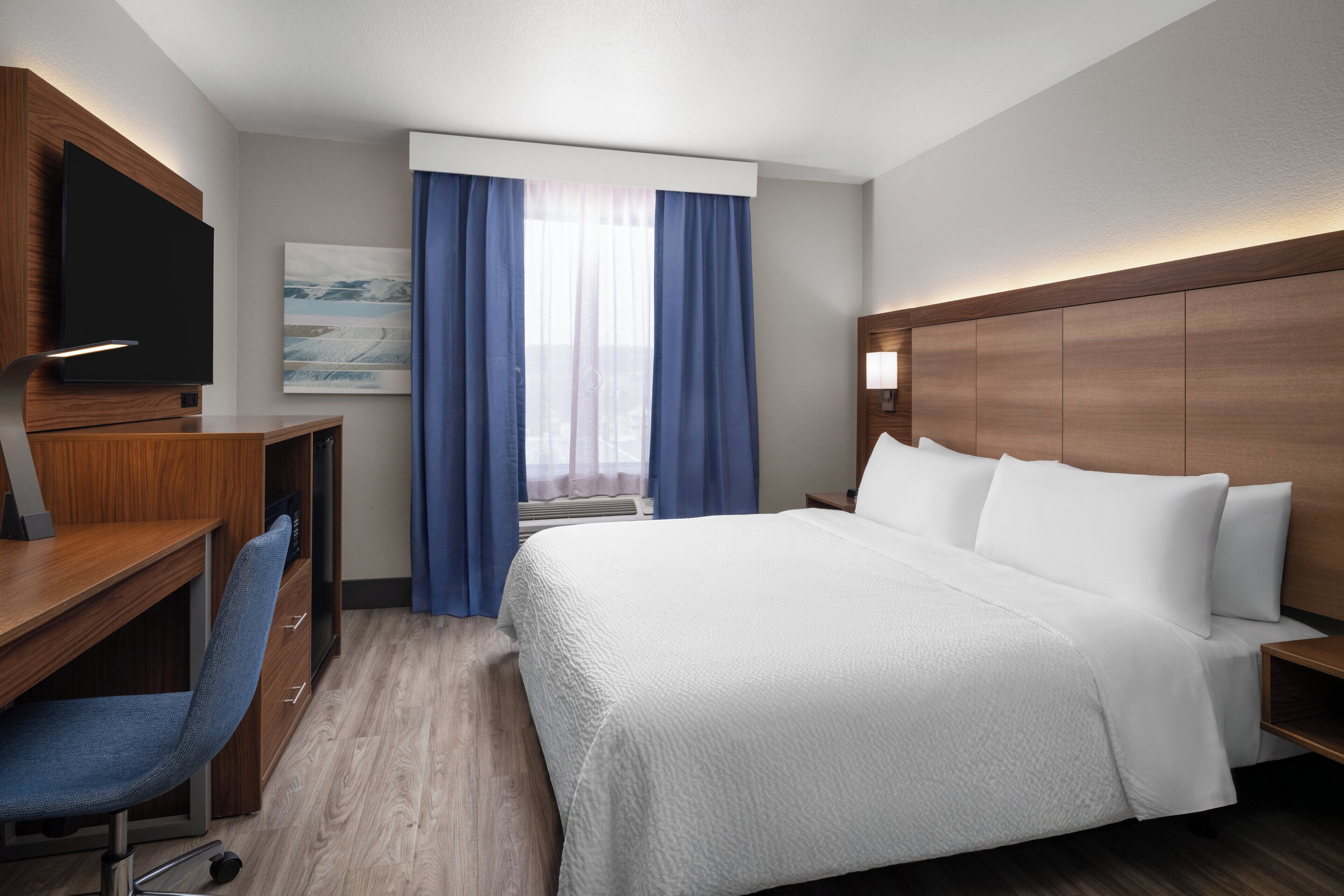 Habitación de hotel con cama, escritorio con silla, televisor de pantalla plana y ventana con cortinas.
