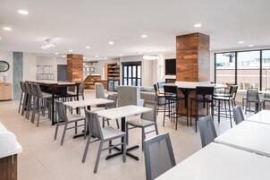 Un restaurante moderno con varias zonas de estar, mesas con sillas y una barra.