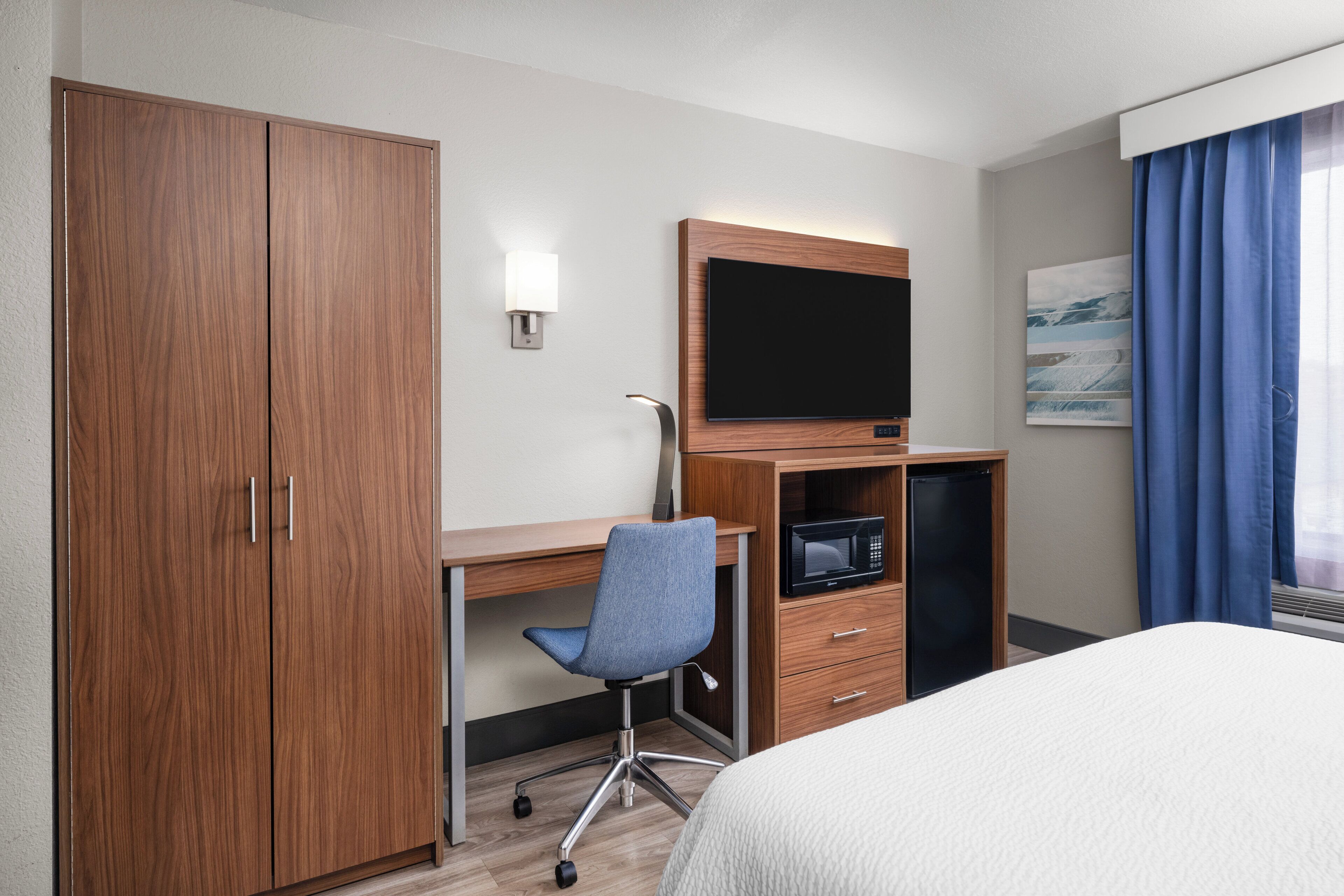 A hotel room with a bed, a desk with a chair, a television, a microwave, and a wardrobe.