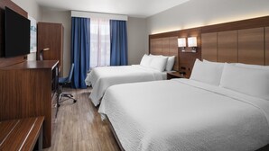 Ein Hotelzimmer mit zwei Betten, einem Schreibtisch, einem Sessel, einem Fernseher und einem Fenster mit Vorhängen.