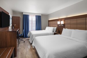 Una habitación de hotel con dos camas, un escritorio, una silla, un televisor y una ventana con cortinas.