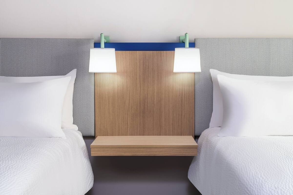 A hotel room with two beds, a wooden headboard, and two bedside lamps.