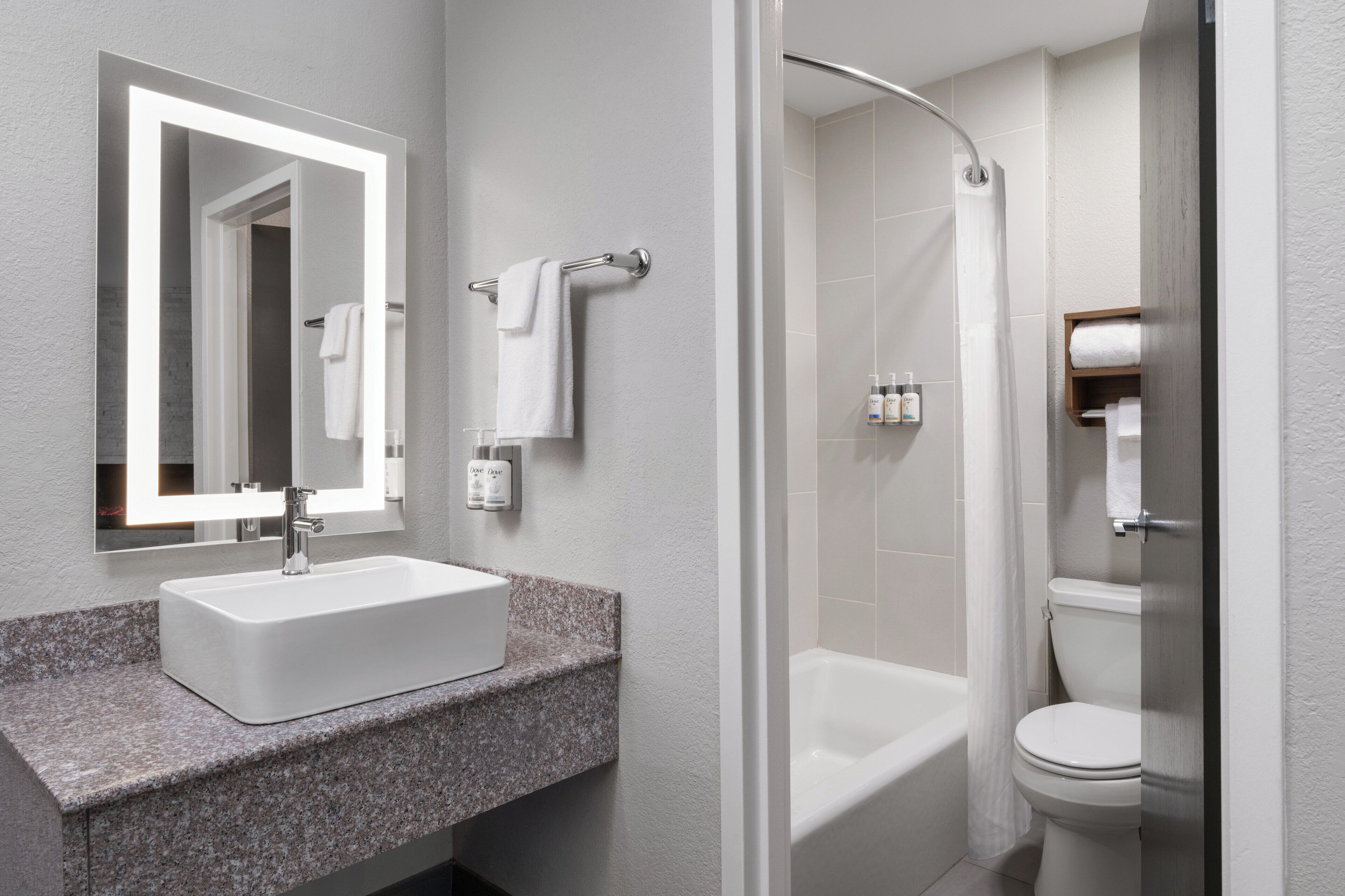 A modern bathroom with a granite countertop sink, a mirror, a shower enclosure, and a toilet.