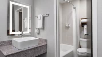 A modern bathroom with a granite countertop sink, a mirror, a shower enclosure, and a toilet.