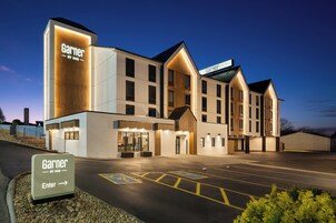 Un hotel con un cartel llamativo de 'Garnier by IHG', un estacionamiento con espacios para discapacitados y una entrada bien iluminada.