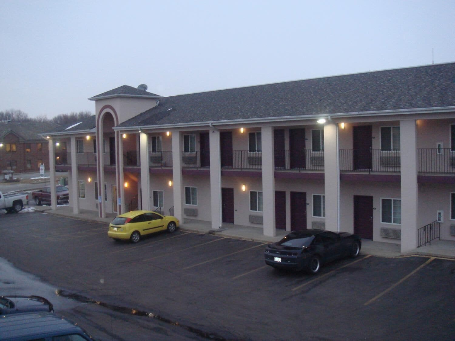 A multi-story motel with a central courtyard, featuring a parking lot with several cars.