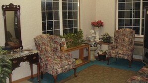 A cozy living room with floral armchairs, a wooden coffee table, a side table with a plant, and a large mirror. - Townhouse Inn & Suites (Omaha)