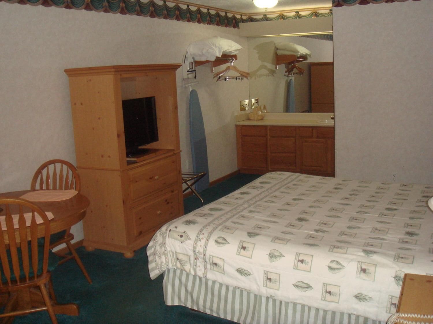 Ein Schlafzimmer mit einem Bett, einem Holzkasten, einem Fernseher, einem Sessel und einem Spiegel.