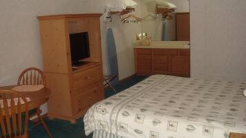 Ein Schlafzimmer mit einem Bett, einem Holzkasten, einem Fernseher, einem Sessel und einem Spiegel.