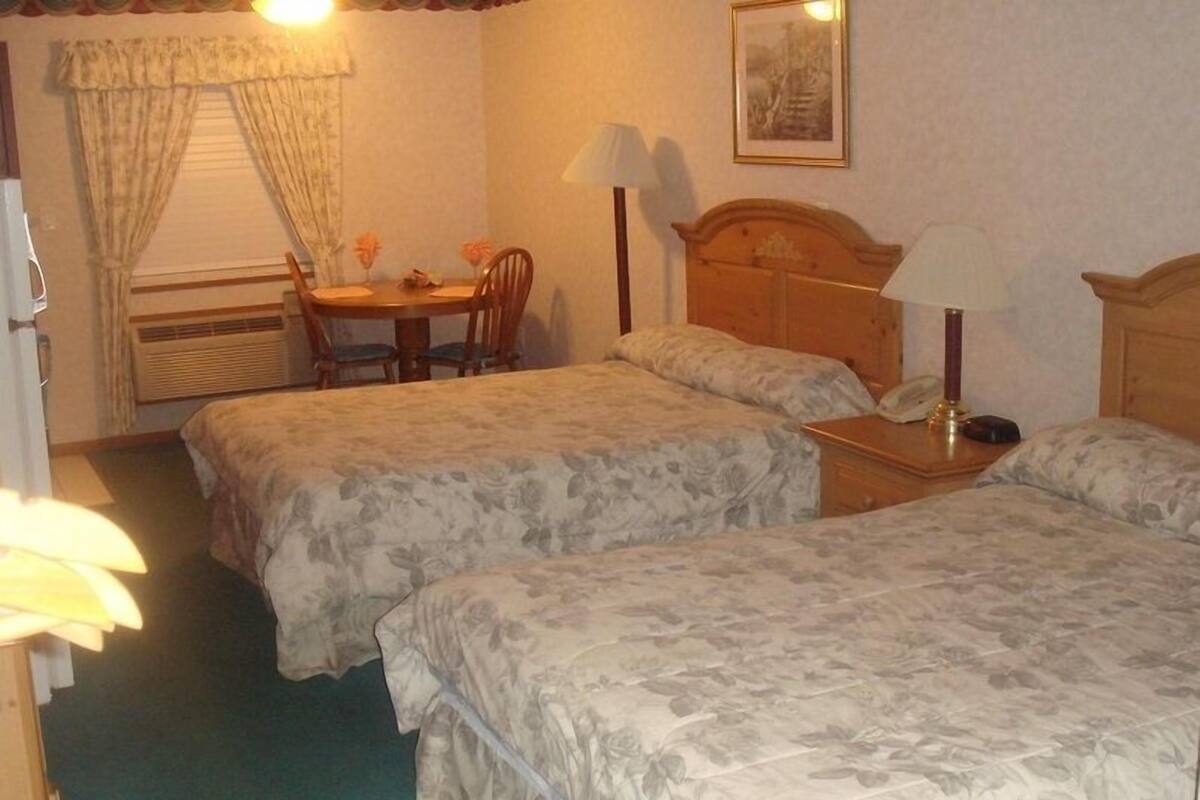 Une chambre d’hôtel avec deux lits, une tête de lit en bois, une petite table avec des chaises et une fenêtre avec des rideaux.