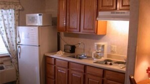 A compact kitchen with wooden cabinets, a refrigerator, a microwave, a toaster, and a coffee maker. - Townhouse Inn & Suites (Omaha)
