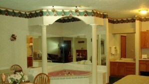 A room with a large bathtub, a dining area with a table and chairs, and a kitchen area. - Townhouse Inn & Suites (Omaha)
