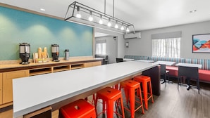 A modern kitchen with a long island, red bar stools, and a seating area with a red sofa and striped cushions. - MainStay Suites Louisville Jeffersontown (Louisville)