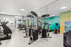 Un gimnasio con diversas máquinas de ejercicio, un dispensador de agua y un espejo grande.