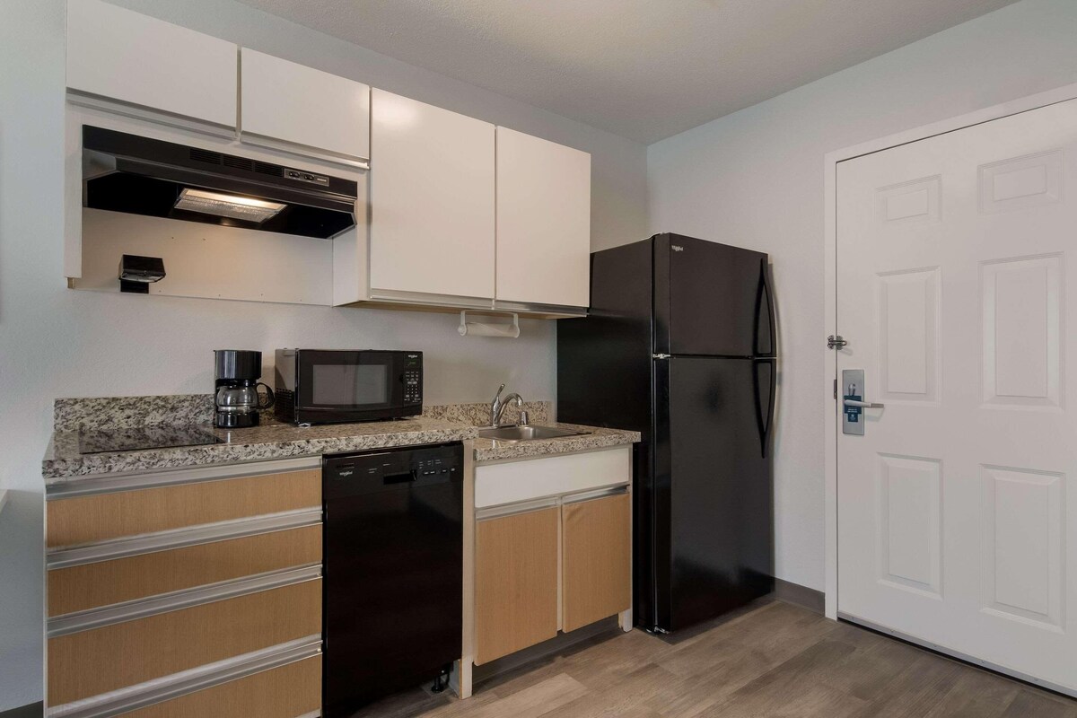 A compact kitchen with a dishwasher, microwave, and black refrigerator.
