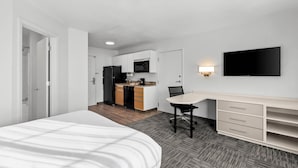 A modern hotel room with a bed, a desk, a chair, a TV, and a kitchenette. - MainStay Suites Louisville Jeffersontown (Louisville)