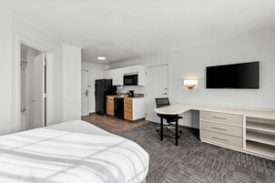 Una habitación de hotel moderna con cama, escritorio, silla, televisor y kitchenette.