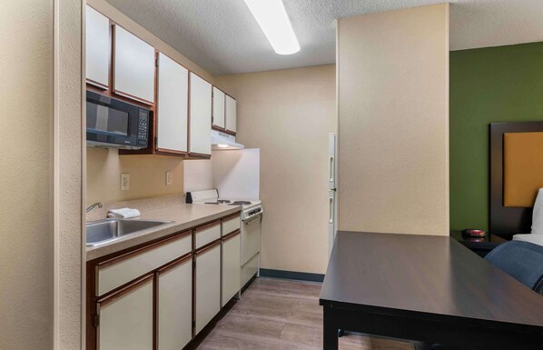 A compact kitchen with a microwave, stove, and sink. A dining table is positioned near the window. - Extended Stay America Select Suites St Louis Earth City (Bridgeton)