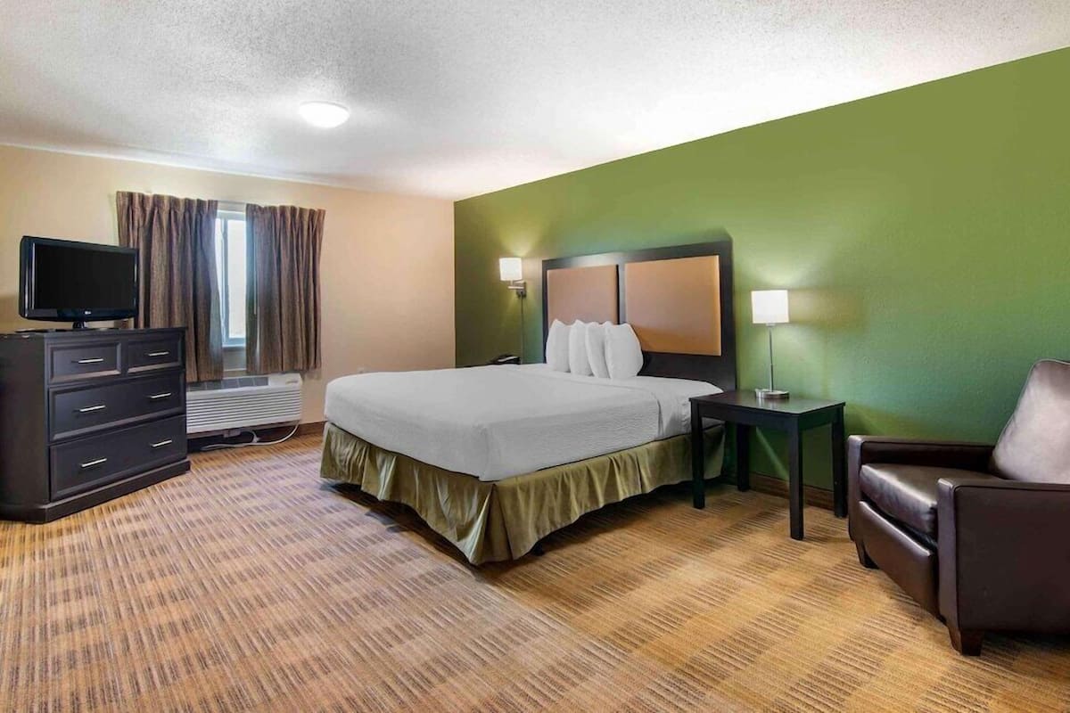 A hotel room with a bed, a TV, a dresser, a chair, and a lamp.