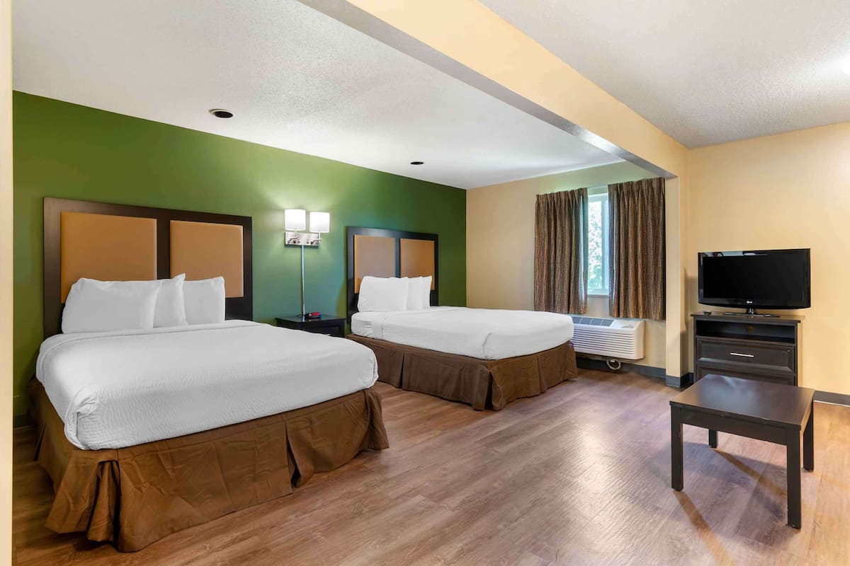 A hotel room with two beds, a TV, a desk, and a window with curtains.