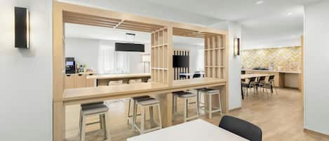 Una habitación de hotel moderna con comedor, televisor montado en la pared y cocina.