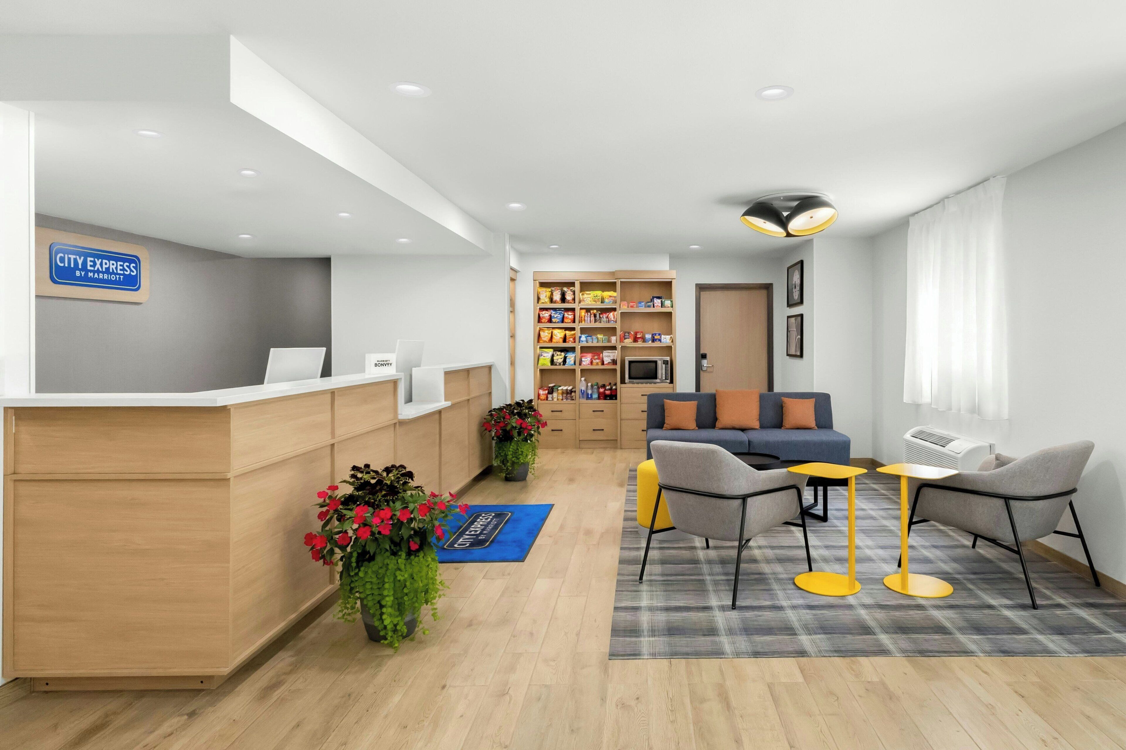 A hotel reception area with a desk, seating, a kitchenette, and a bookshelf.