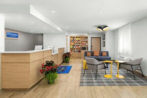 Un espace d’accueil d’hôtel comprenant un comptoir, des sièges, un coin cuisine et une bibliothèque.