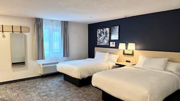 A hotel room with two beds, a large mirror, a window with curtains, and artwork on the wall.