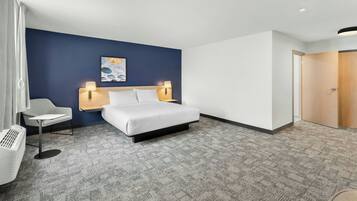A hotel room with a bed, bedside lamps, a chair, a small table, and a wall-mounted artwork.