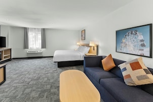 A hotel room with a bed, a sofa, a desk, a television, and a large window with curtains.
