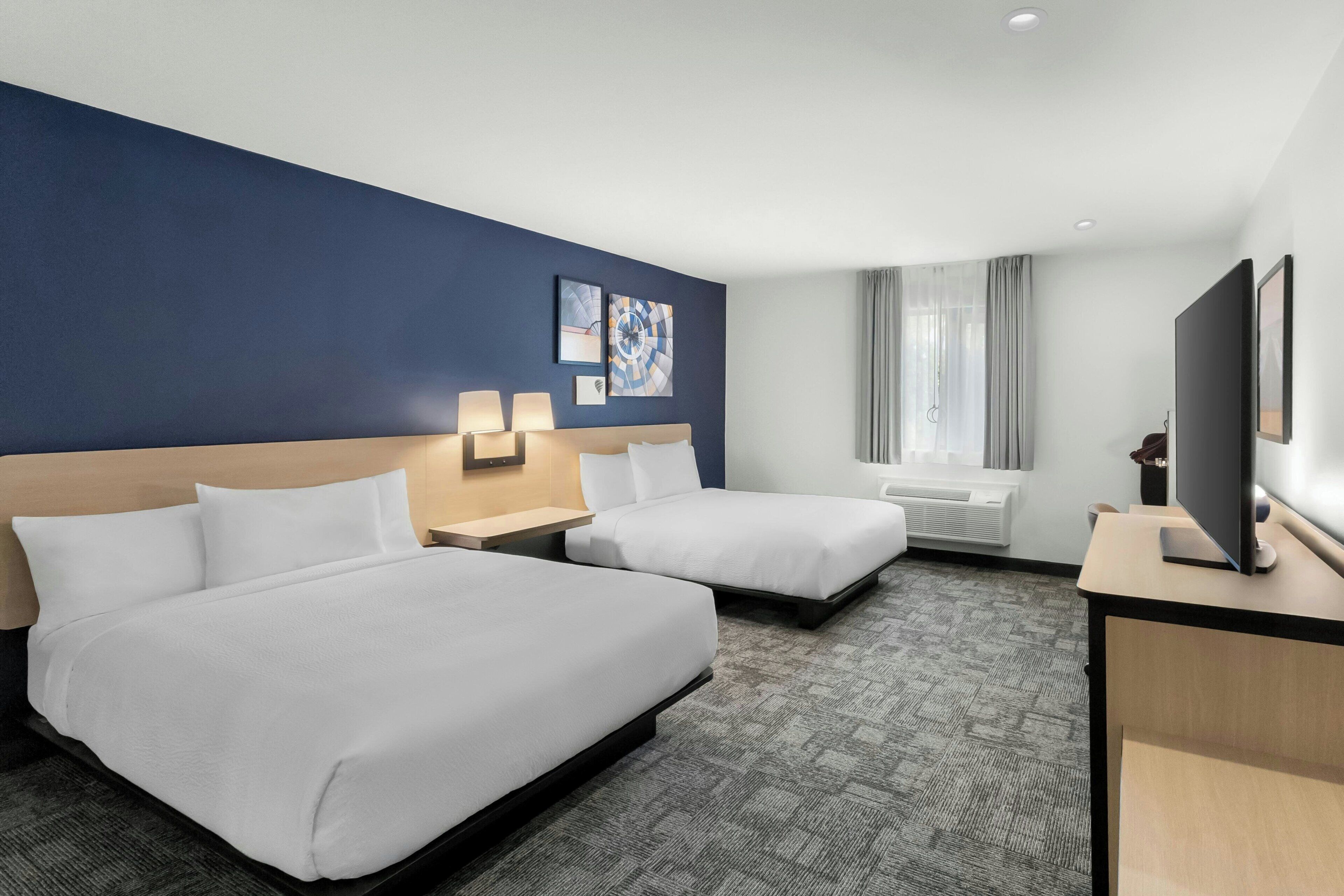 A hotel room with two beds, a desk, a television, and a window with curtains.