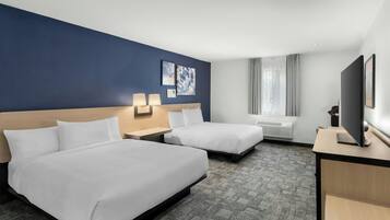Habitación de hotel con dos camas, un escritorio, un televisor y una ventana con cortinas.