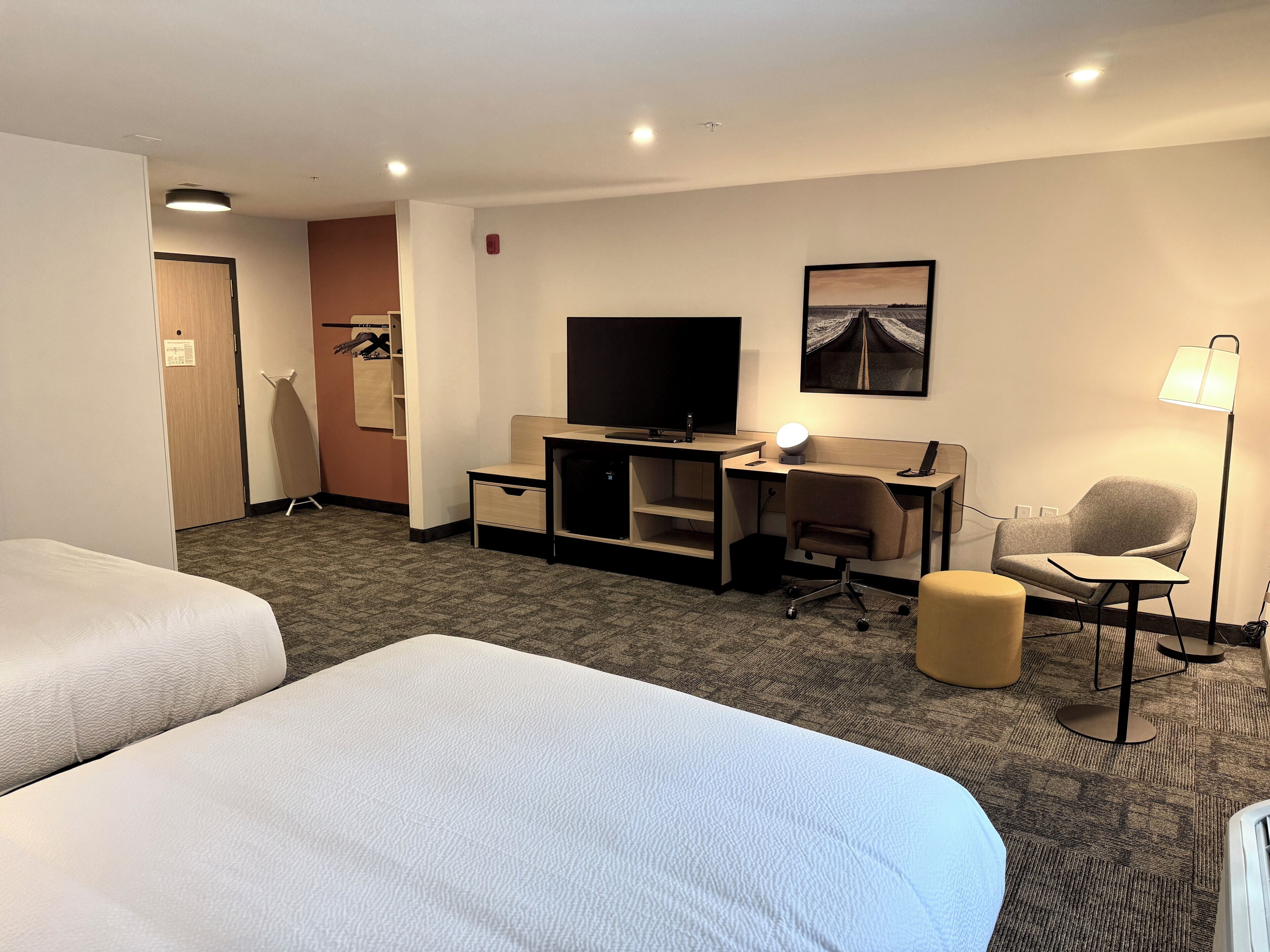 Habitación de hotel con dos camas, un escritorio, una computadora, una silla, una lámpara y un televisor.