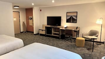 Habitación de hotel con dos camas, un escritorio, una computadora, una silla, una lámpara y un televisor.