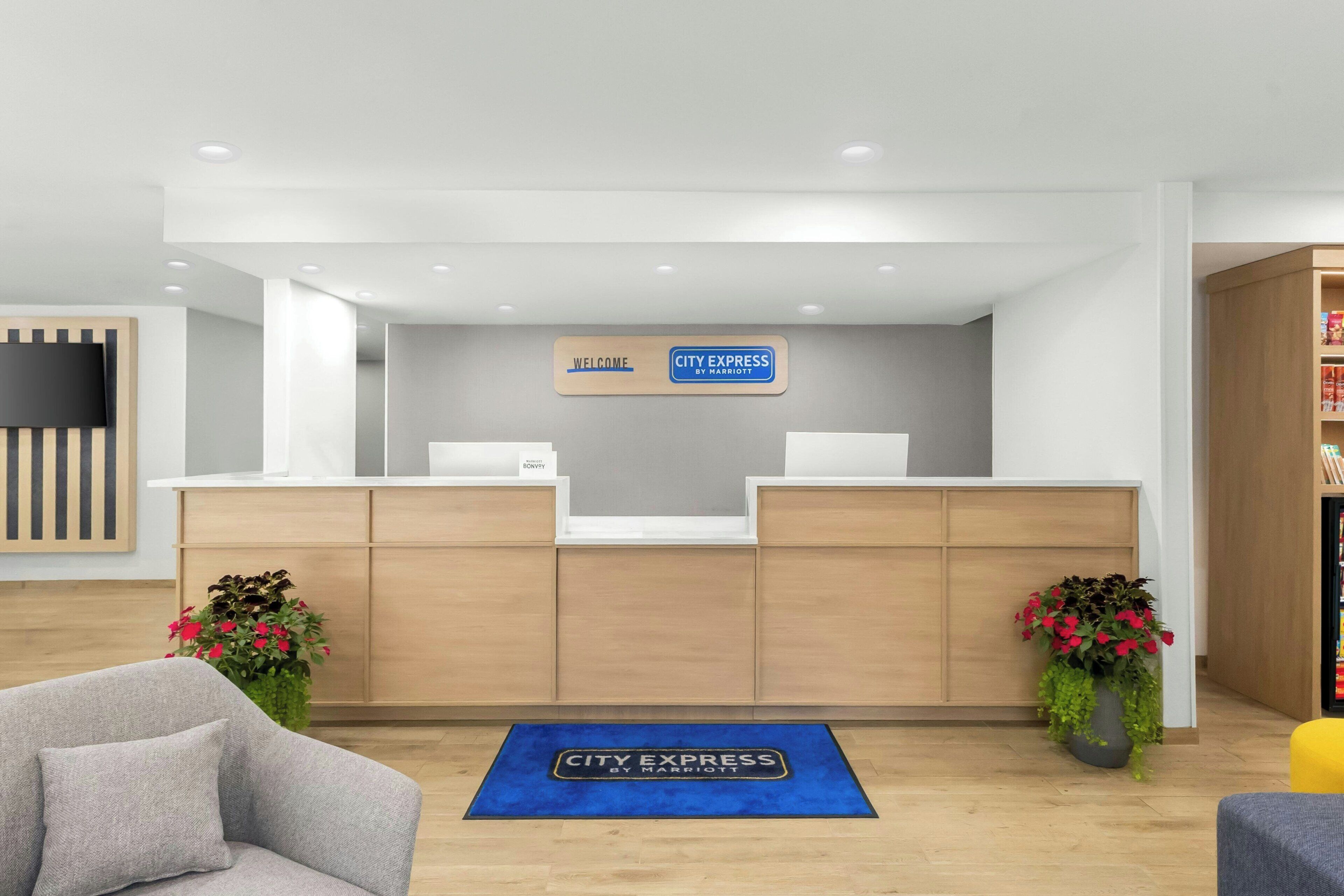 A hotel reception area with a modern design, featuring a reception desk, a welcome sign, and a blue mat on the floor.