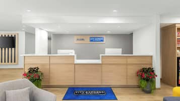 A hotel reception area with a modern design, featuring a reception desk, a welcome sign, and a blue mat on the floor.