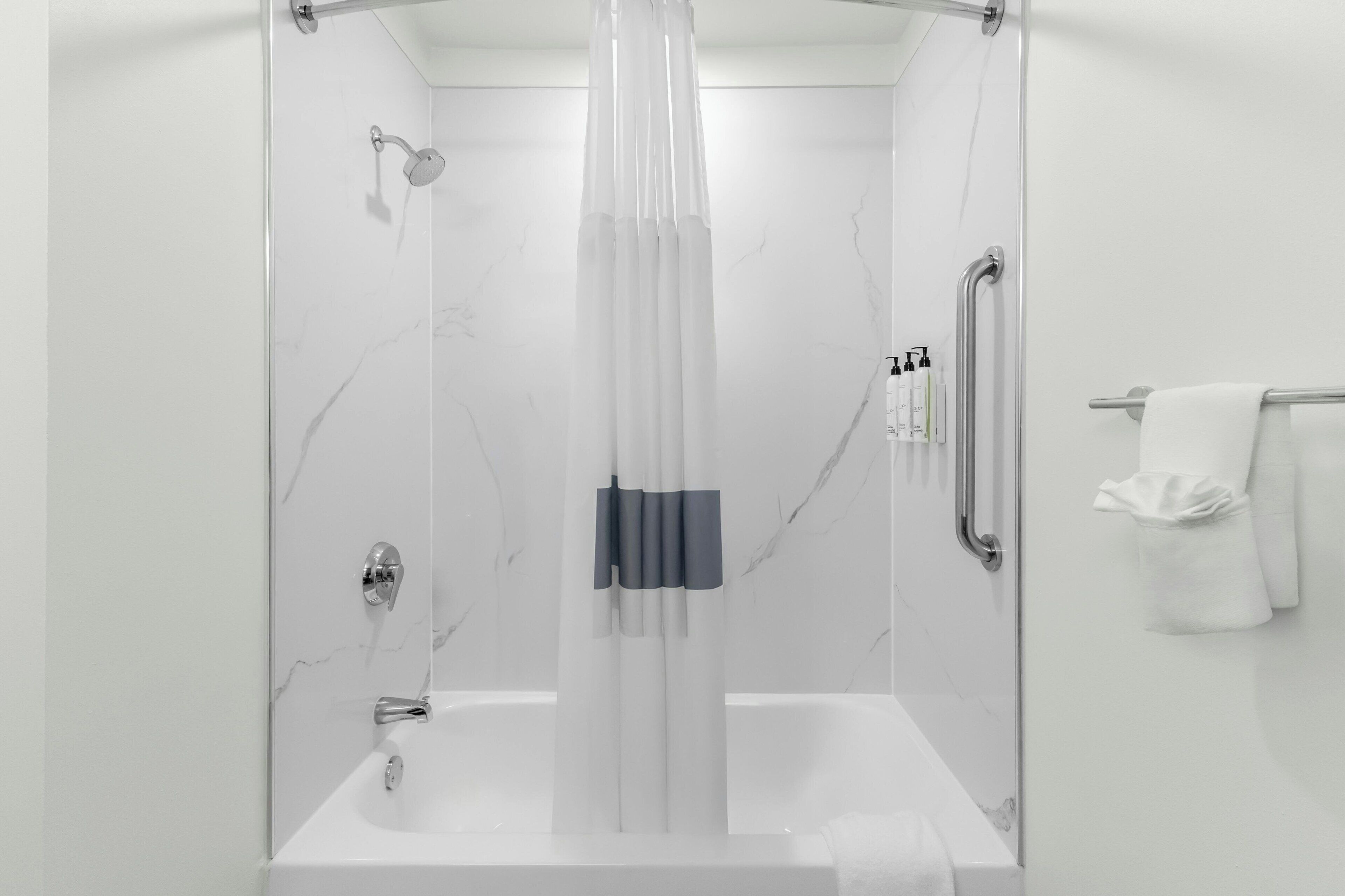 A modern bathroom with a glass-enclosed shower, a white bathtub, and a towel rack with towels.